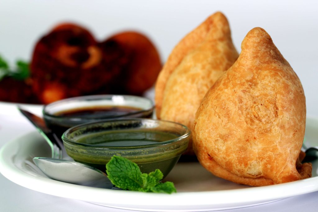 Popular indian, asian and african deep fried snack called samosa with spicy chutney and mint