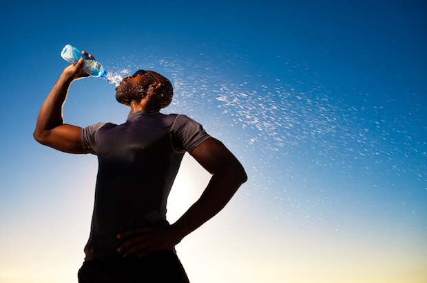 Silhouette of a man drinking water after exercising with blue sky in the background.
